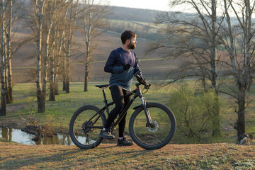 Cyclist in shorts and jersey on a modern carbon hardtail bike with an air suspension fork standing on a cliff against the background of fresh green spring forest