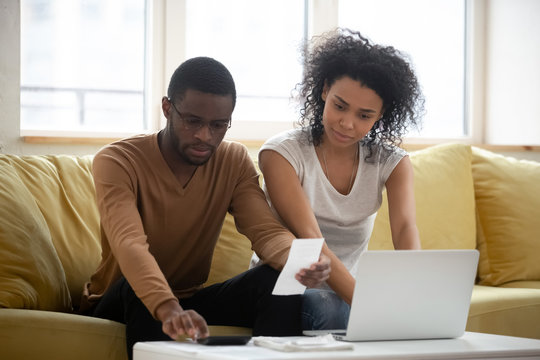 Serious African American Couple Using Calculator And Laptop For Calaulating Finance. Diverse Upset Man And Woman Taxing, Accounting With Check Credit Analytic For Mortgage Payment.