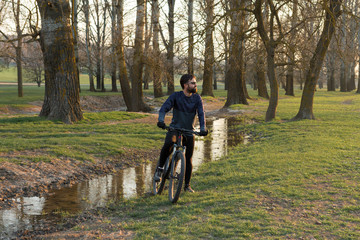 Fototapeta premium Cyclist in shorts and jersey on a modern carbon hardtail bike with an air suspension fork standing on a cliff against the background of fresh green spring forest