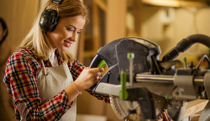 portrait of young caucasian carpenter working in workshop listening to music, woman enjoy making...