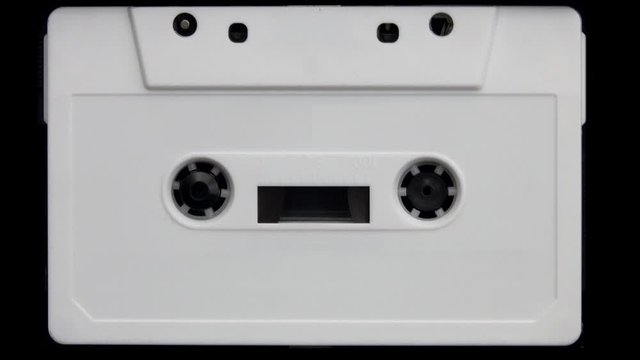 A vintage and unlabeled white analog cassette tape plays in a closeup view.