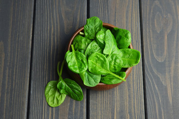 Fresh spinach leaves in wooden bowl over old wooden table. Healthy vegan food. Green living and eco-conscious concept.