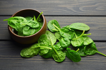 Fresh spinach leaves in wooden bowl on dark rustic background. Healthy vegan food concept. Eco-conscious vegan lifstyle.