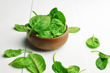 Fresh spinach leaves in wooden bowl over white wooden table. Healthy vegan food. Green living and eco-conscious concept.