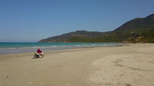 a flying camera takes pictures of a girl riding a motorbike in the sand on the beach. Nha Trang Vietnam