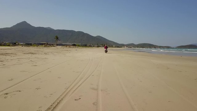 a flying camera takes pictures of a girl riding a motorbike in the sand on the beach. Nha Trang Vietnam