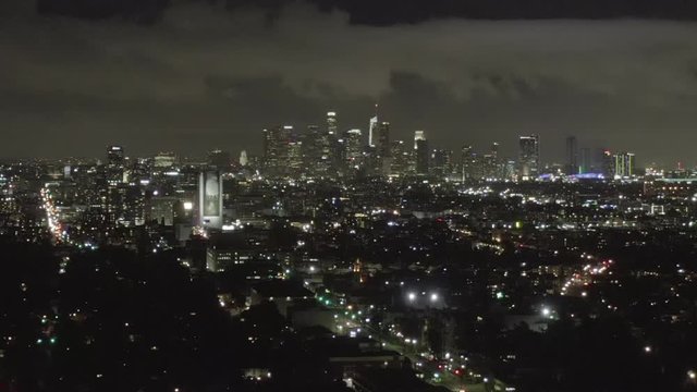 AERIAL: Over Dark Hollywood Los Angeles at Night with Clouds over Downtown and City Lights 