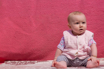 Fototapeta premium Little adorable blonde baby girl sit on carpet and this cute baby looking to the somewhere, outside activity