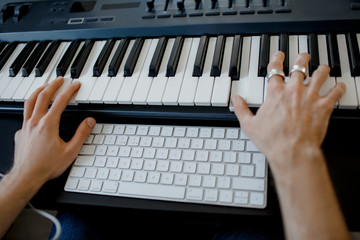 Fototapeta na wymiar composer hands on piano keys in recording studio. music production technology, man is working on pianino and computer keyboard on desk. close up concept.