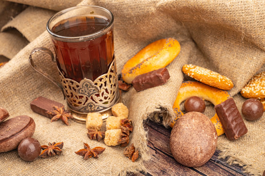 A faceted glass of tea in a vintage Cup holder, bagels, cookies and chocolate gingerbread on a background of fabric with a rough texture. Close up.