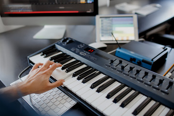 composer hands on piano keys in recording studio. music production technology, man is working on pianino and computer keyboard on desk. close up concept.