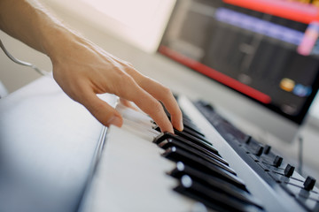 composer hands on piano keys in recording studio. music production technology, man is working on pianino and computer keyboard on desk. close up concept.