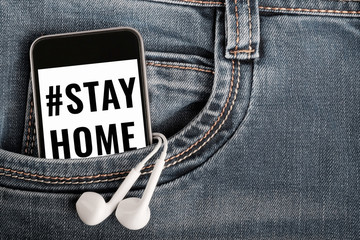 modern smartphone and earphones on denim textile. text on phone screen encourages stay at home to prevent virus infection