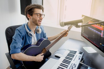 Man plays guitar and singing and produce electronic soundtrack or track in project at home. Male...