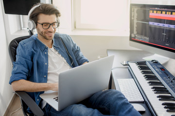 Working on a laptop. Busy guy. Multitasking concept. DJ in broadcasting studio. music producer is composing a song on synthesizer keyboard and computer in recording studio.