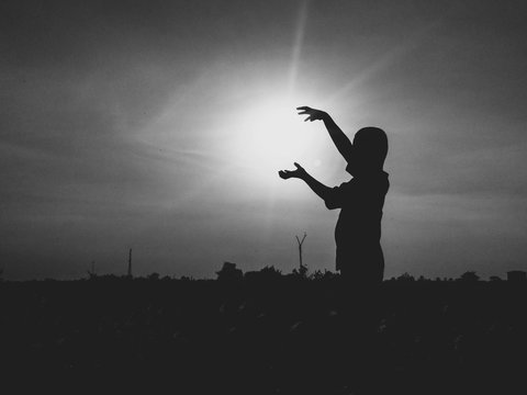 Optical Illusion Of Silhouette Boy Holding Sun While Standing On Field Against Sky