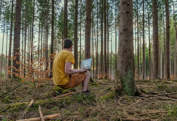 Fototapeta premium Enjoying work on the fresh air, a man works with his laptop in a natural looking forest.