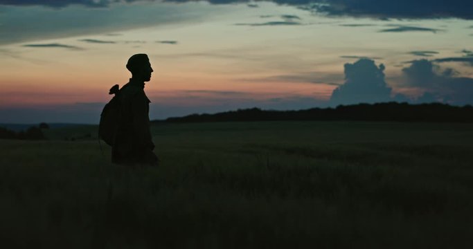 Silhouette of lonely soldier walking in field on red sunset background. A sad conceptual scene about the history of the soldiers of World War II and the Cold War.