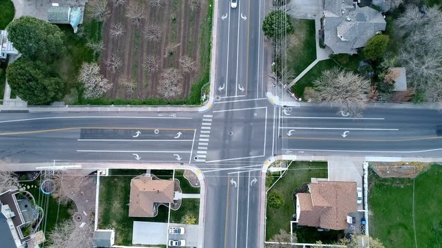 Circling over intersection as 2 cars stop and continue to drive from aerial view above.