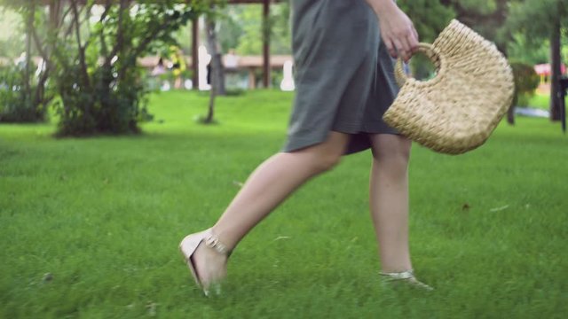 Side view of Young woman with handmade stylish straw handbag walks in the summer park. Eco bag.