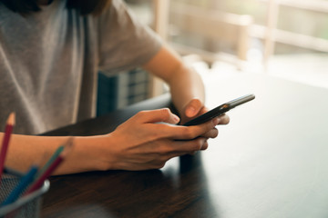 Closeup of young woman hand holding smartphone and chatting with friends at social network on the table in cafe.
