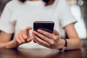 Closeup of young woman hand holding smartphone and chatting with friends at social network on the table in cafe.