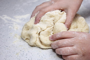 Children's hands knead a piece of dough. The process of kneading the dough