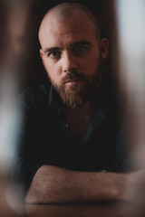 Obraz premium Attractive bald man with long redhead beard and blue eyes looking to the camera. Wearing blue shirt. Photo with sparkles, high contrast, and low saturation and blurs contrast. 