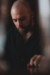 Obraz premium Attractive bald man with long redhead beard and blue eyes looking to the camera. Wearing blue shirt. Photo with sparkles, high contrast, and low saturation and blurs contrast. 