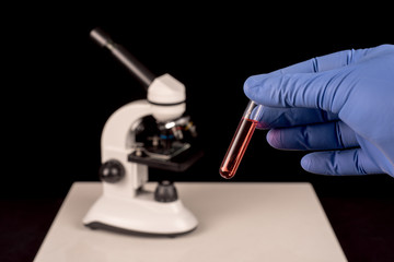 Microscope blurred and hand with surgical glove holding vial with red solution. Black background with space for text