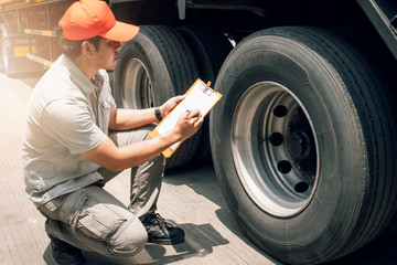 Asian truck driver holding clipboard inspecting safety check a truck tire, vehicle maintenance...
