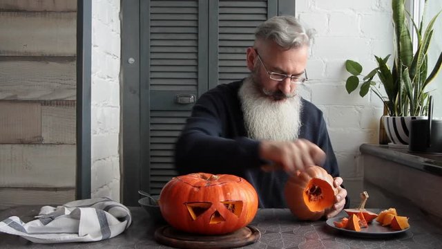 Caucasian mature bearded man makes pumpkin lantern Jack-o-lantern, markup and cut out his eyes and mouth, Halloween concept