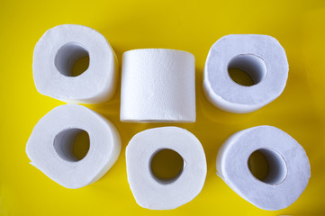 Pile of rolls of white toilet paper on a yellow background, top view