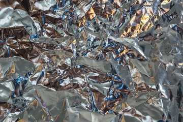 Abstract crumpled reflective silver material with blue and yellow light background