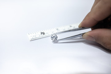 Hand holding a diamond with linear scale, tweezers and a pile of diamond. Worker measures the size of gems on a jewelry scale isolated on white background.