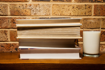 Stack of books and a glass of milk against a brick wall