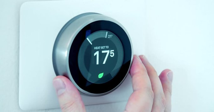 A person using a Smart Thermostat with a hand setting lower the temperature saving energy