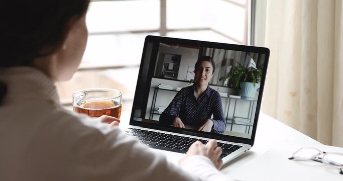 Young female remote worker video conference calling indian manager on laptop screen working from home office distance meeting using online computer chat software concept. Over shoulder closeup view