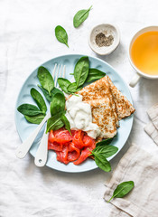 Delicious breakfast - crepes with smoked salmon, spinach, cream fresh on a light background, top view