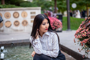Fototapeta premium happy Asian business woman with long black hair wearing a trendy corporate shirt and skirt is sitting confidently at an outdoor park enjoying the view of Chicago downtown