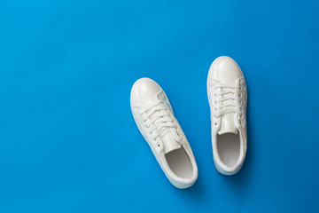 Classic white athletic sneakers on a blue background. Sports style. Flat lay.