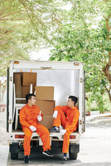 Tired movers sitting in loaded van trunk, drinking water and talking during short break