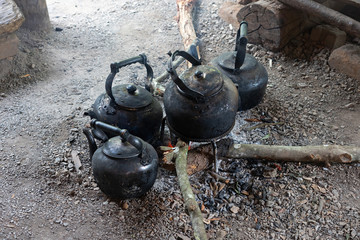 Old kettles covered with black soot on bonfire with woods