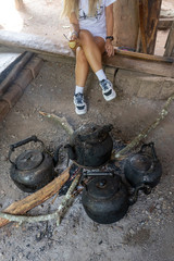 Old kettles on bonfire with asian woman holding coffee cup