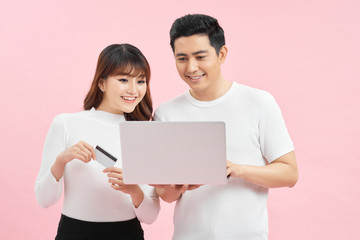 Great credit offer. Cheerful asian couple shopping online on laptop with bank card on pink studio background