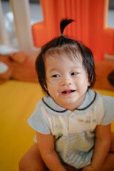 Baby girl smiles and look around in children partitions on doll background. Cute daugther looks at camera ,so happy time with family at home.