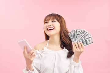 Image of a shocked surprised screaming young pretty woman posing isolated over pink wall background using mobile phone holding money.