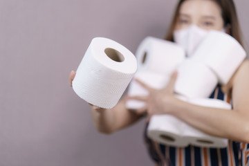 Woman stocking up toilet paper for home quarantine, holds many rolls of toilet paper in hand.