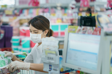 Woman protects herself from corona infection with surgical mask and gloves at cashier scanning grocery .