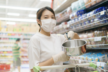 Woman wearing surgical mask and gloves,  buying stainless steel pot in supermarket. Panic shopping after coronavirus pandemic.